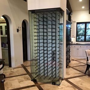 A modern glass-enclosed wine rack with black metal supports stands in a stylish kitchen featuring tile flooring, white cabinets, and sleek design. This custom glass wine cellar adds an elegant touch to the space, perfect for displaying bottles. A modern glass-enclosed wine rack with black metal supports stands in a stylish kitchen featuring tile flooring, white cabinets, and sleek design. This custom glass wine cellar adds an elegant touch to the space, perfect for displaying bottles.