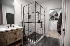 Modern bathroom with frameless shower doors featuring black grid lines, a wooden vanity with a sink on the left, dark floor tiles, and an adjacent walk-in closet with white drawers for added bathroom appeal.